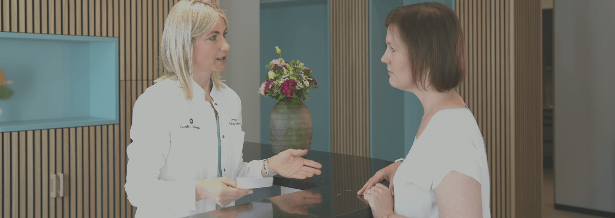 Foto: Dr. med. Catharina Hamm (links) an der Rezeption im Gespräch mit einer Patientin (rechts)