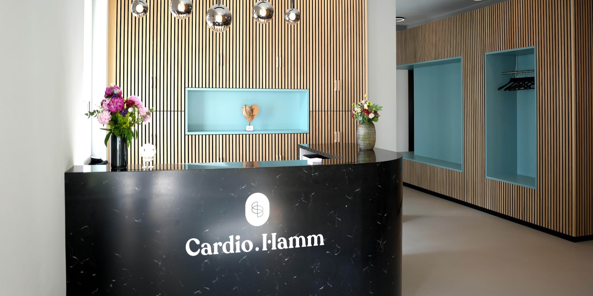 Foto des modernen und hochwertigen Eingangsbereichs der kardiologischen Privatpraxis Cardio.Hamm in Bad Nauheim. Sicht auf die Theke und Garderobe