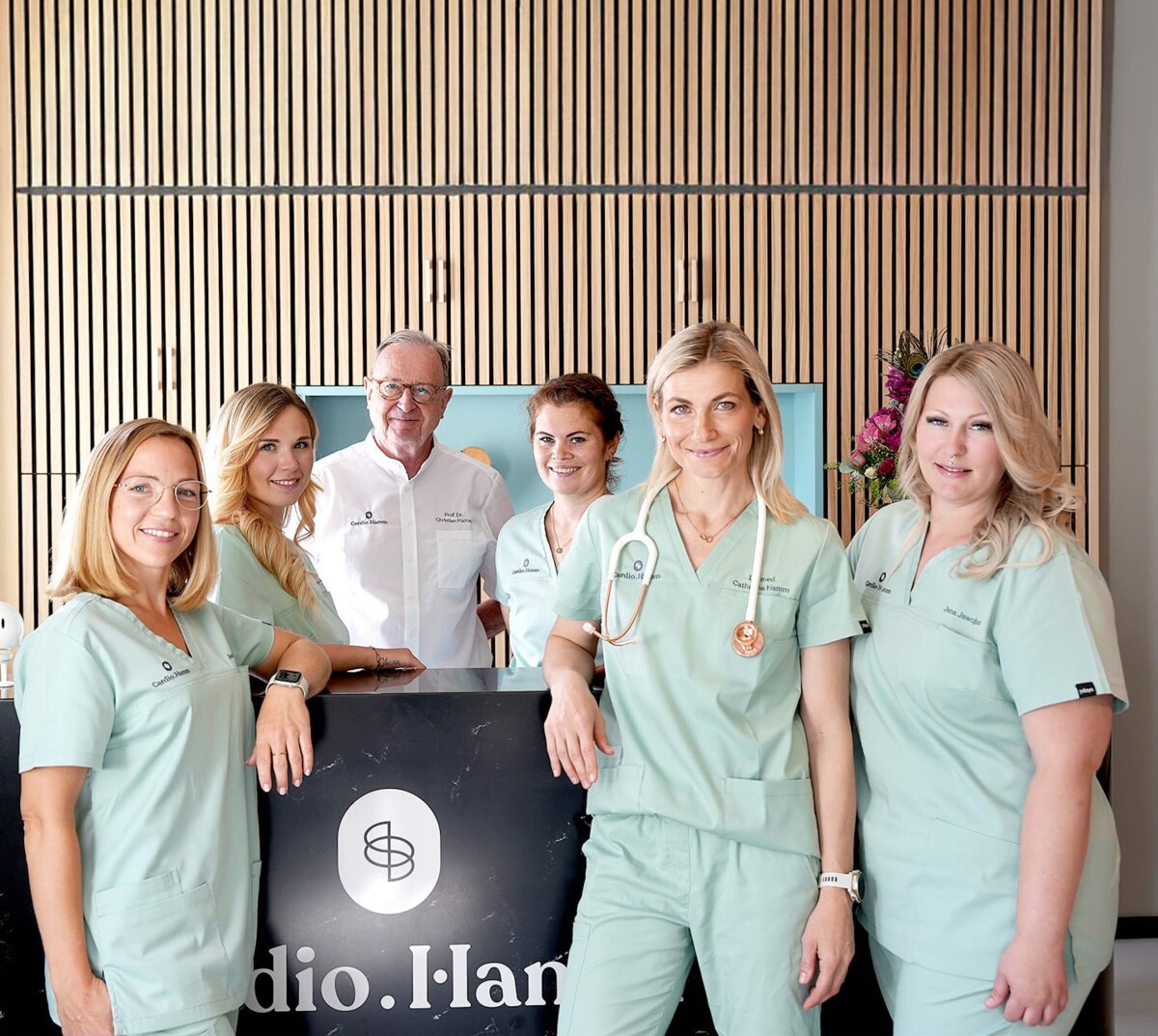 Das sympathische Team von Cardio.Hamm in Bad Nauheim steht an der Rezeption der Praxis und lächelt freundlich in die Kamera