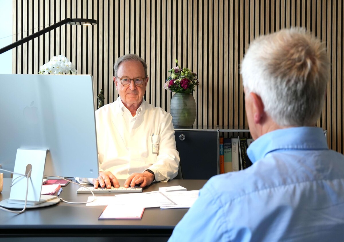 Foto: Prof. Dr. med. Christian Hamm sitzt einem Patienten am Bürotisch gegenüber